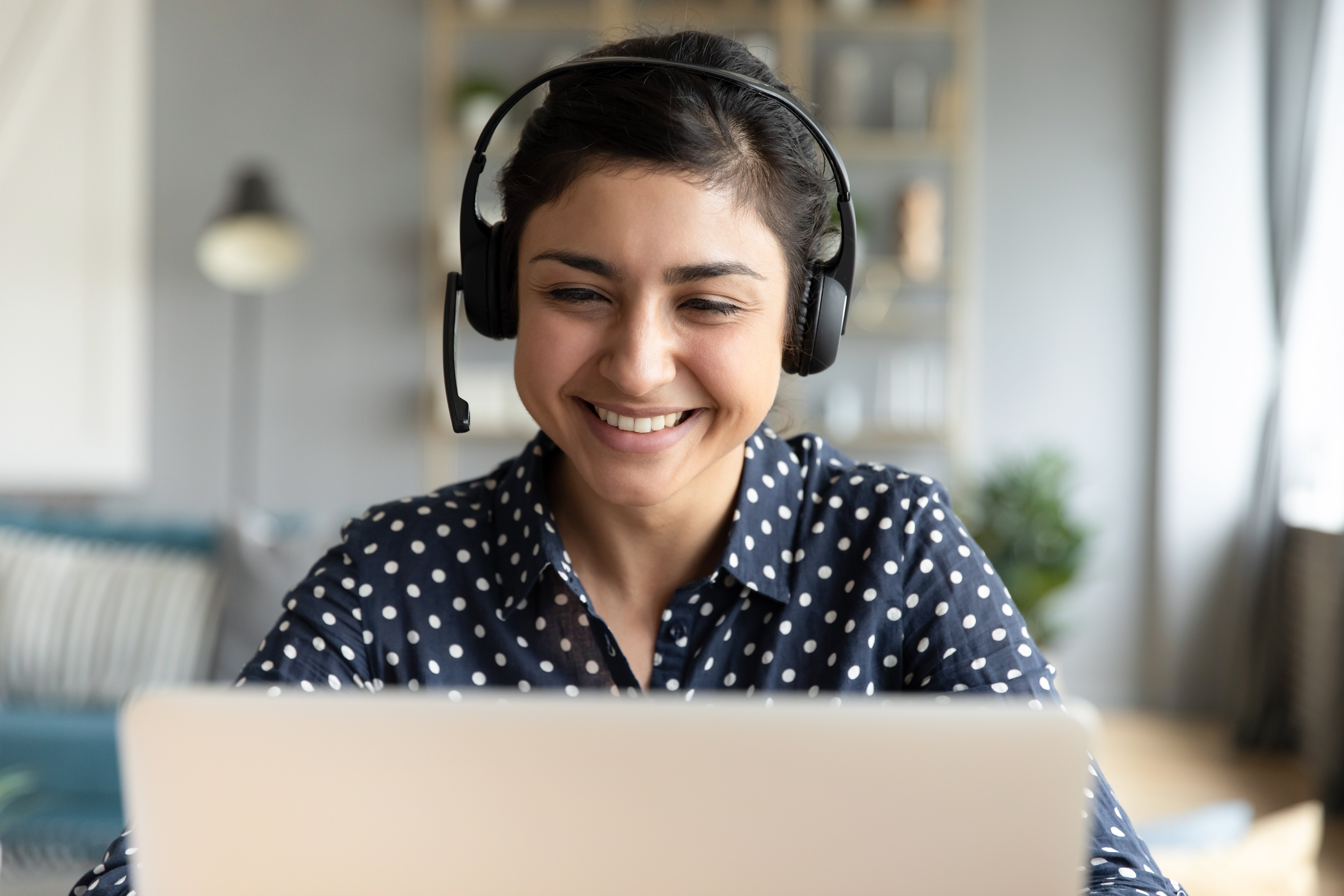 Lächelnde Frau trägt ein Headset und schaut auf Laptop-Bildschirm