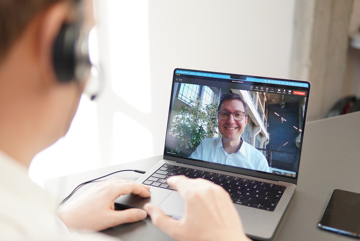 Teilnehmer einer Videokonferenz schaut lächelnd aus dem Bildschirm den Vertriebsmitarbeiter an